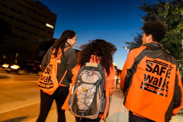 Two SAFEwalk staff (in bright orange) walk with a student as the night begins.