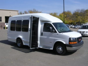Image of the left side of the white bus, shot from the front. Loading door is open and UW decals are visible.