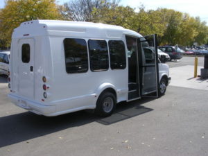 Image of the left side of the white bus, shot from the back. Loading door is open and UW decals are visible.