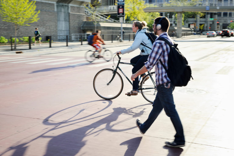 A pedestrian and bicyclist use a crosswalk on University Avenue on a sunny spring day.