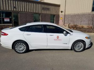White Ford Fusion hybrid electric sedan with UW decals.