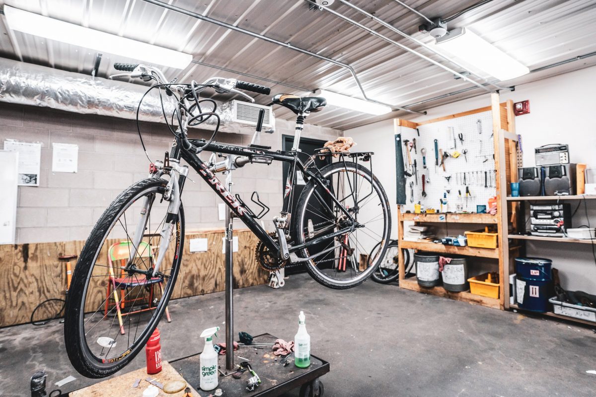 A black bicycle is elevated on a stand so it can be worked on. Interior of the University Bicycle Resource center is visible; a tool bench can be seen in the background.