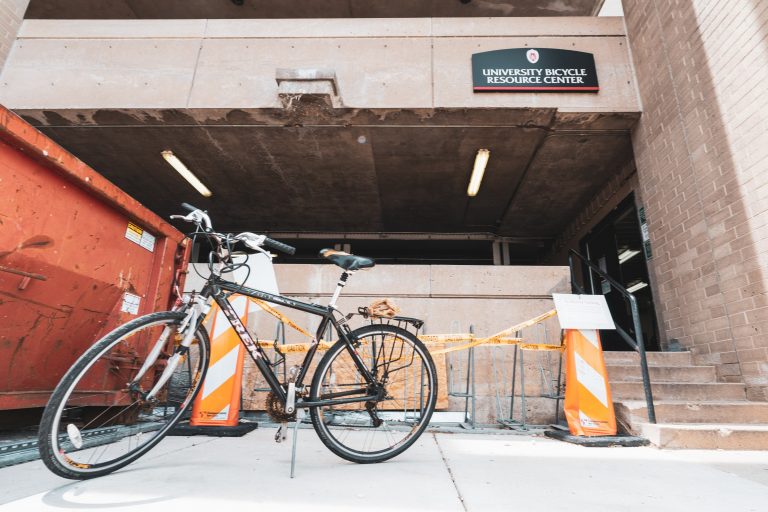 An image shot from below of a black bicycle displayed in front of the lower level of Lot 6, where a sign for the University Bicycle Resource Center is visible in the background.