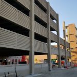 View from the ground of the side of the new partially constructed parking structure, lacking several panels and glass.