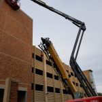 A tall, articulated lift crane is helping construct the side of the parking garage.