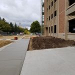 Street level image showing fresh sidewalk running along side the under-construction new parking facility.