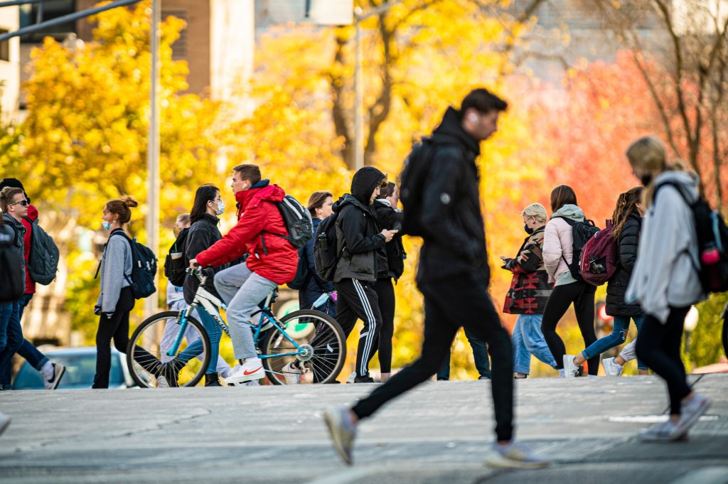 This image shows several UW students walking and biking across a busy intersection on University Avenue on a fall day. The image shows how many members of the campus community use multiple forms of active transportation to get around on campus.
