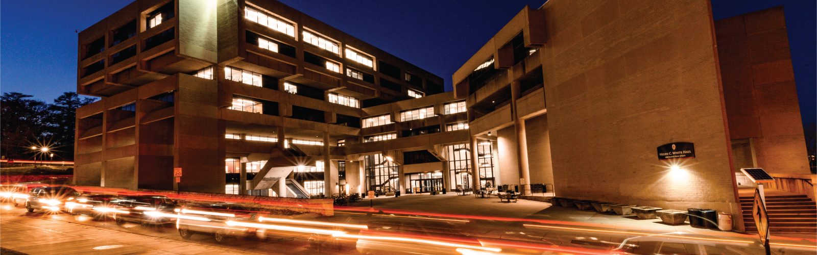 Photo of Helen C White Hall at night with traffic on Observatory Drive.