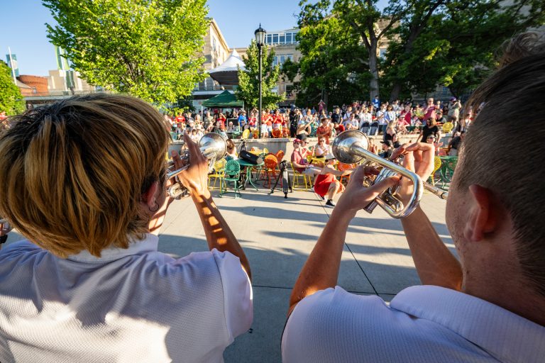 Photo of UW Marching Band members playing trumpets in front of a crowd on the Memorial Union Terrace in spring 2023.