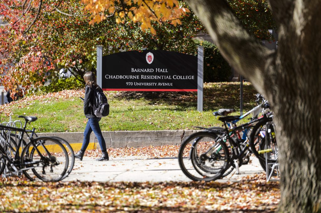 Image of a student walking near several bikes parked at bike racks in front of Chadbourne Residence Hall on the UW-Madison campus.