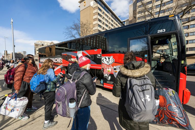 Photo of students gathering along the Lake Street sidewalk near Gordon Dining and Event Center to board buses headed to destinations such as Minneapolis and airports in Chicago and Milwaukee as the spring recess is set begin at the University of Wisconsin–Madison.